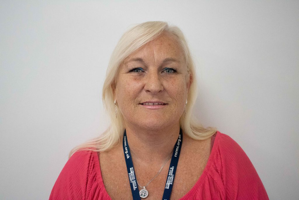 Headshot of Paula Bramble, shoulder-length blond hair, pink top, security pass strap around neck.